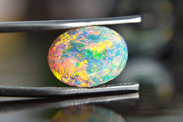 Ein ovaler Opal wird von einer Zange gehalten
