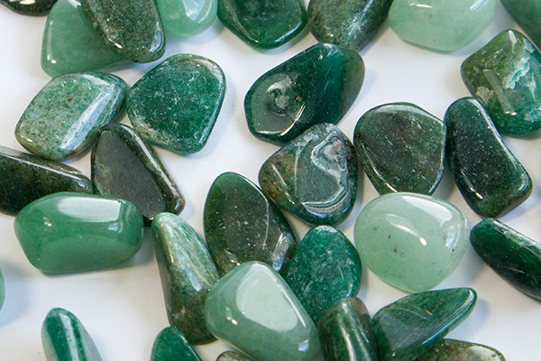 Several aventurine gemstones in various shades of green and shapes on a white surface