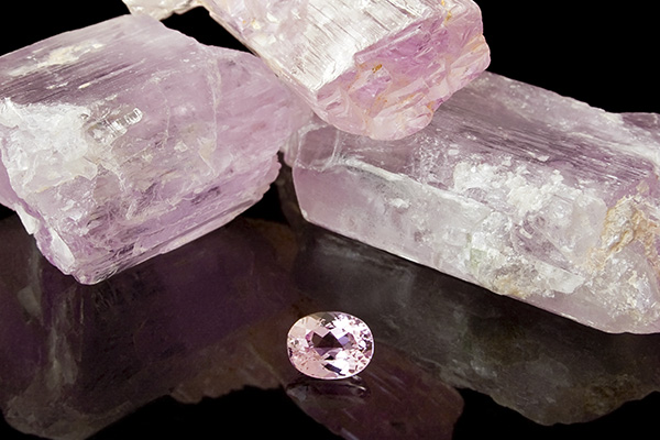 Three naturally grown kunzite stones and a faceted kunzite on a black background
