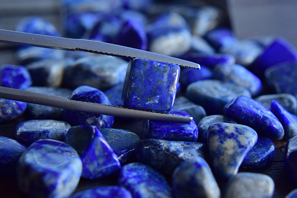 A lapis lazuli held by pliers against a background of other lapis lazuli stones