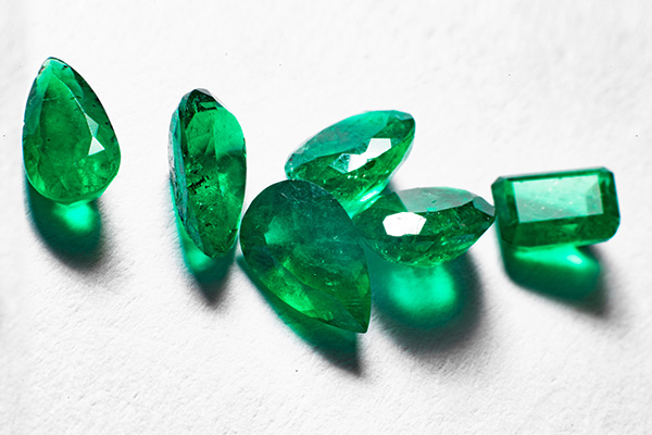 Differently cut emeralds on a light surface casting shadows