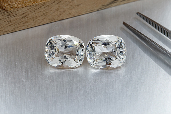 Two faceted white topazes lying on a table next to a large jeweler's tweezers